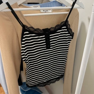 Randig linne  - Säljer ett supersnyggt randigt linne. Det är svartvitt med spetsdetaljer vid halsringningen och knappar framtill. Perfekt för sommardagar eller som ett lager under en jacka. Passar både till vardags och fest!