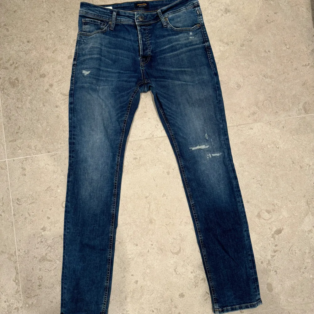 Blåa jeans från Jack & Jones i storlek 32W och L32, med trendiga slitningar för en snygg, avslappnad look. Skick 8/10 – jeansen är i gott skick med lätt slitage som ger extra karaktär. Hör gärna av dig vid minsta funderingar!. Jeans & Byxor.