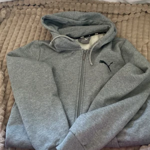 Grå hoodie från Puma - Säljer en grå hoodie från Puma i mycket bra skick. Den har en dragkedja framtill och en klassisk huva. Perfekt för höst och vinter, och den är supermjuk och bekväm. Passar både för träning och vardagsbruk. 🐾