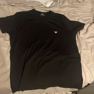 Svart t-shirt från Armani Exchange - Säljer en stilren svart t-shirt från Armani Exchange i storlek M. Den har en liten vit logga på bröstet och är perfekt för både vardag och fest. T-shirten är i mycket bra skick och gjord av mjukt material för en bekväm passform.