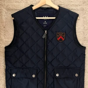 Mörkblå quiltad väst från Morris - Säljer en snygg mörkblå quiltad väst från Morris i mycket bra skick. Västen har en dragkedja framtill och två fickor med knappar. Perfekt för höst och vår. Passar bra till både casual och lite mer uppklädda tillfällen.