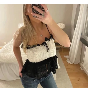 Vit och svart stickad topp med volangdetaljer - Snygg vit och svart stickad topp från Zara med tunna axelband och volangdetaljer. Toppen har en dekorativ knytning framtill och är perfekt för en trendig look.