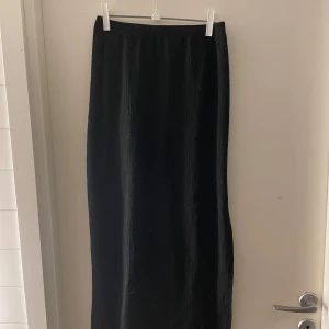 Svart långkjol från Shein - Snygg svart långkjol från Shein i ett stilrent och enkelt utförande. Kjolen har en slits som ger en extra touch och är perfekt för olika tillfällen. Tillverkad i ett bekvämt material som passar bra till både vardag och fest.