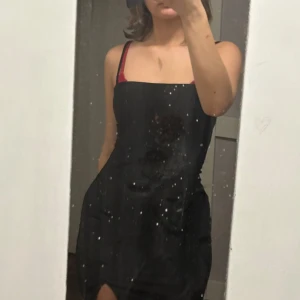 Svart glittrig klänning med smala axelband - Snygg svart klänning med glittrigt material och smala axelband. Perfekt för en kväll ute eller en speciell tillställning. Klänningen har en tight passform som framhäver figuren.