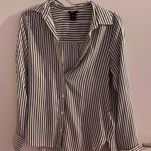 Randig skjorta från lindex - Snygg och stilren randig skjorta från lindex i svart och vit. Skjortan har långa ärmar och knappar framtill. 