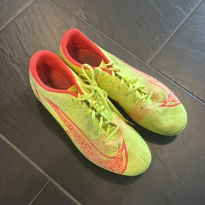 Gula fotbollsskor från Nike - Säljer ett par gula fotbollsskor från Nike med röda detaljer och snörning. Skorna har en lätt och smidig design med dobbar för bra grepp på planen. Perfekta för den som vill ha stil och funktion i ett.