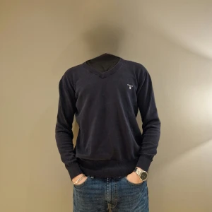 Mörkblå tröja från GANT - Säljer en stilren mörkblå tröja från GANT med v-ringning och broderad logga på bröstet. Tröjan har långa ärmar och är tillverkad i ett mjukt material som passar perfekt för kyligare dagar. Vid funderingen är det bara att höra av sig// Merch Åled 