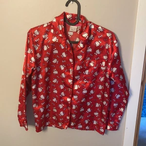 Röd Hello Kitty pyjamas i satin - Säljer en superfin röd Hello Kitty pyjamas i satin. Skjortan har långa ärmar och knappar framtill. Byxorna har en bekväm resår i midjan. Perfekt för mysiga kvällar hemma! 💤