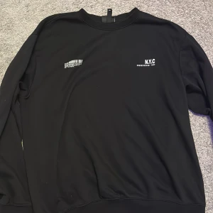 Svart långärmad tröja med NYC-tryck - Säljer en svart långärmad tröja med tryck av texten 'N.Y.C' och 'Brooklyn' på bröstet. Tröjan har en avslappnad passform och är perfekt för en casual look. Passar bra till jeans eller joggers.