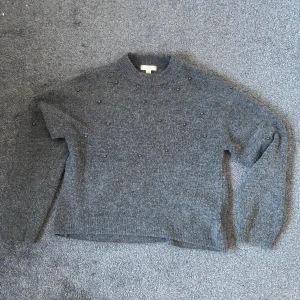 Grå ulltröja med pärlor - Säljer en mysig grå ulltröja dekorerad med små pärlor. Tröjan har långa ärmar och ribbstickade kanter vid ärmslut och nederkant. Perfekt för kyliga dagar! Passar både Xs/S. 