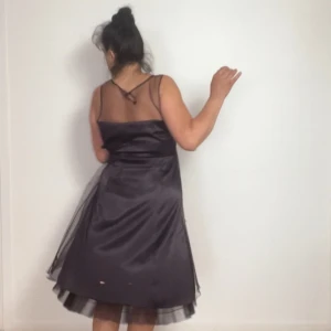 Mörkt lilla fest klänning med tyll - Elegant mörkt lilla festklänning med tyll och transparenta axelband från VILA  Den har en fin A-linjeformad siluett och är perfekt för festliga tillfällen. Klänningen har en subtil glans och flera lager som ger volym.