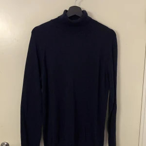 Mörkblå polotröja från Bläck - Säljer en stilren mörkblå polotröja från Bläck. Perfekt för kyligare dagar med sin höga krage och långa ärmar. Tröjan är i en klassisk design som passar till många tillfällen. Tröjan är aldrig använd och prislapp finns kvar.