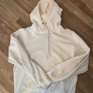 Vit hoodie - Säljer en klassisk vit hoodie med justerbar dragsko i huvan. Perfekt för en avslappnad stil och passar till det mesta. Den har långa ärmar och en bekväm passform.