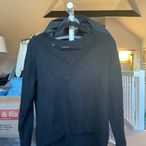 Svart stickad tröja med v-ringning - Säljer en svart stickad tröja med v-ringning. Tröjan har långa ärmar och en klassisk design som passar perfekt för kyligare dagar. Perfekt för lager-på-lager-stil eller att bära som den är.