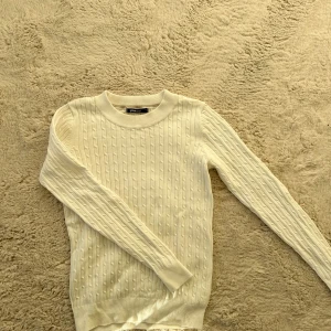 Vit stickad tröja från Gina Tricot - Säljer en stilren vit stickad tröja från Gina Tricot. Tröjan har ett klassiskt flätmönster och långa ärmar. Perfekt för kyligare dagar. Passar till många olika outfits!