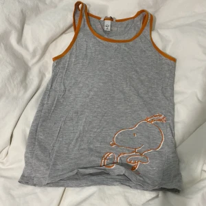 Grå linnetopp med orange kant - Säljer en grå linnetopp med orange kant och ett tryck av Snoopy i nedre hörnet. Perfekt för en avslappnad stil. Mysig att sova i, pris kan diskuteras
