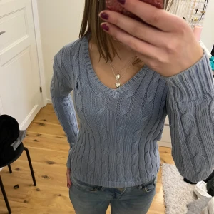 Äkta Ralph Lauren! Stickad tröja - Säljer en ljusblå stickad tröja med kabelstickat mönster. Tröjan har en v-ringad hals och långa ärmar, perfekt för kyligare dagar. Passar bra till jeans eller kjol för en avslappnad look.