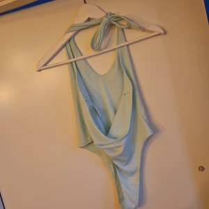 Mintgrön body med knytband - Snygg mintgrön body med knytband i nacken. Den har en stilren design med en djup urringning och öppen rygg.