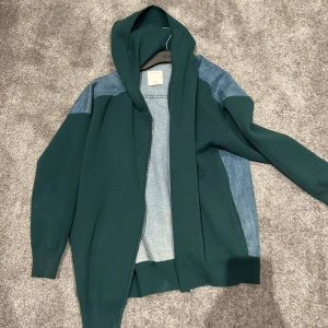 Grön och blå jacka med huva från Sandro - Snygg jacka från Sandro i en cool kombination av grönt tyg och blå denim. Jackan har en huva och dragkedja framtill. Jackan är använd fåtal gånger och är lite oversized i modellen.