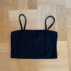 Svart randig crop top - Snygg svart tubtopp med smala axelband och vita ränder. Perfekt för en stilren look. Passar både till vardag och fest.