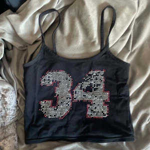 Svart linne med strassdetaljer från Mouth Valley - snyggt svart linne från mouth valley med tunna axelband och ett stort '34' med diamanter på framsidan. köpte secondhand men aldrig använt. en del diamanter saknas utöver det är de bra skick