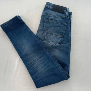 Blå jeans från Jack & Jones - Snygga blå jeans från Jack & Jones med en lätt slitning för en cool look. De har en klassisk femficksdesign och knappgylf. Perfekta för en avslappnad stil. Modellen: Slim Glenn. Storlek 30/30