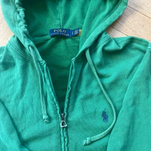 Grön hoodie från Ralph Lauren - Säljer en snygg grön hoodie från Ralph Lauren med dragkedja och huva. Den har en broderad logga på bröstet och är perfekt för en avslappnad stil. Passar bra till jeans. Zip up hoddien är köpt på Nk Göteborg vid Polo Ralph lauren så den är äkta💕Zip up hoddien är perfekt för lite kyligare vår/ sommarkvällar och för sommarstugan🌷hoddien är knappt använd . priset kan självklart diskuteras! 