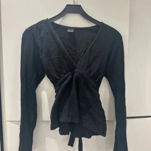 Svart omlottopp med knytband - Snygg svart omlottopp från Zara med långa ärmar och knytband i midjan. Perfekt för en stilren look. Toppen har en v-ringad design som ger en elegant touch.