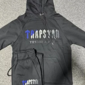 Svart hoodie från Trapstar - Säljer en svart Trapstar hoodie med blått och grått tryck. Klassisk passform med huva och ribbade muddar. Perfekt för en avslappnad stil!