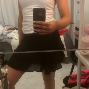 Svart kortkjol med volang - Säljer en svart kortkjol med volangdetaljer. Kjolen har en luftig och lekfull design som passar perfekt för varmare dagar. Den är enkel att matcha med olika toppar och accessoarer.