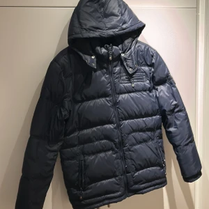 Mörkblå dunjacka med huva - Säljer en snygg mörkblå dunjacka från EDC. Jackan har en avtagbar huva med knappar där bak. En väldigt snygg och bra jacka för er som gillar monclers sortiment då den liknar en Maya. Jackan är i storlek XL men passar mig som är ungefär 185.