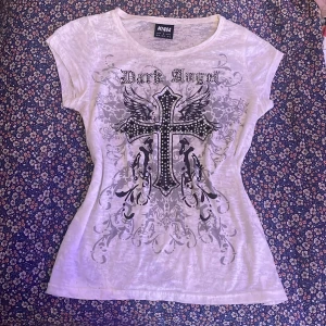 Vit t-shirt med tryck från Minga London - Säljer en cool vit t-shirt från Minga London med ett stort tryck av ett kors och texten 'Dark Angel'. T-shirten har korta ärmar och ett unikt mönster med detaljer i svart och grått💘