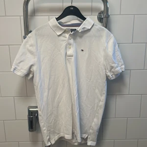 Vit pikétröja från Tommy Hilfiger - Säljer en klassisk vit pikétröja från Tommy Hilfiger. Tröjan har korta ärmar och en liten logotyp på. Nytt skick på denna med. Försöker frakta samma dag 