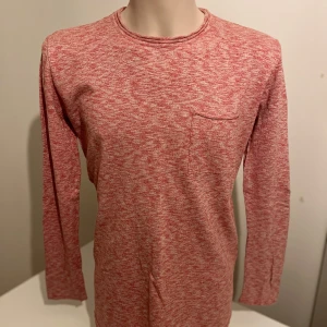 Rödmelerad långärmad tröja från WINWIN - Säljer en rödmelerad långärmad tröja från WINWIN. Tröjan har en enkel bröstficka och en rund halsringning. Perfekt för en avslappnad stil. 🧶