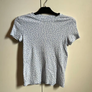 Ljusblå ribbad topp från Monki - Säljer en ljusblå ribbad topp från Monki med ett blommigt mönster i vitt. Toppen har korta ärmar och en rund halsringning. Skriv för fler bilder eller funderingar💕