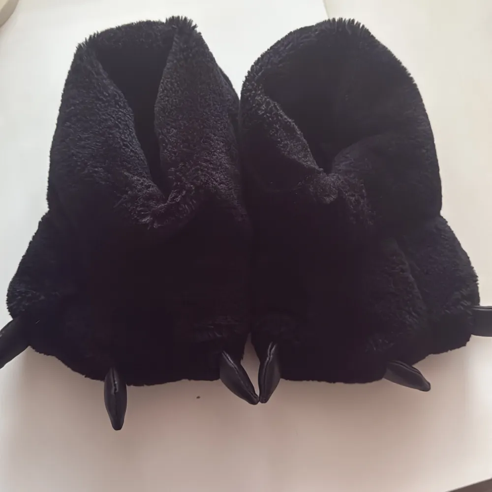 Mysiga svarta tofflor i plyschmaterial med kloliknande detaljer framtill. Perfekta för att hålla fötterna varma och ge en rolig touch till hemmastilen. Sulan är mönstrad för bättre grepp.. Kengät.