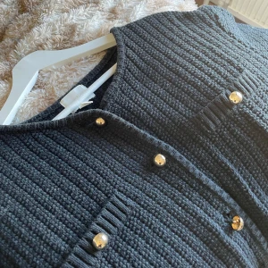 Svart stickad kofta med guldknappar från h&m  - Säljer en elegant svart stickad kofta med korta ärmar och guldiga knappar. Koftan har en ribbad struktur och två dekorativa fickor framtill. Har använt va 2 gånger och är i fint skick!💕💕