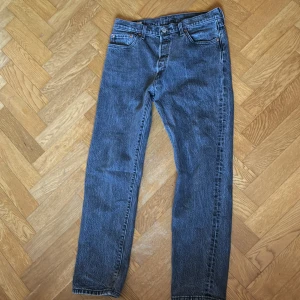 Levis 501 - Klassiska gråa jeansbyxor med en rak passform. De har en traditionell femficksdesign och knappar i midjan. Perfekta för en avslappnad stil.