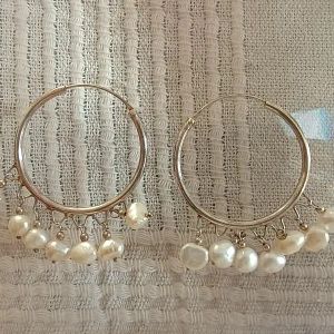 Silverörhängen med pärlor - Stilrena silverfärgade hoop-örhängen dekorerade med hängande vita pärlor. Perfekta för att ge en elegant touch till din outfit. De har en enkel och tidlös design som passar till många tillfällen.