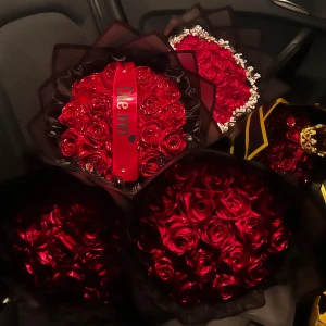 Bukett med glittriga röda rosor - En vacker bukett med glittriga röda rosor, dekorerad med ett svart och rött band med texten 'Dile min'. Rosorna är arrangerade i en elegant svart förpackning som ger en lyxig känsla.