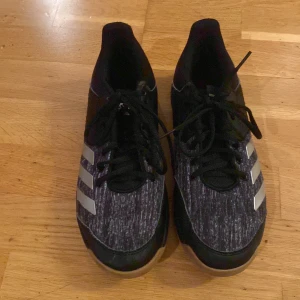 Svarta inomhus skor från Adidas  - Snygga svarta inomhus skor från adidas lite använda men som gott som nya. Skorna har en tjock sula som dämpar väldigt bra när man hoppar och ska landa bra och stadigt. Tjocka sidor av skorna så att man sällan får ont när man springer i skorna och gör olika aktiviteter. 