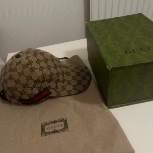 Beige canavas gucci keps  - Säljer en snygg beige canavas keps från Gucci med det klassiska GG-mönstret. Kepsen har en justerbar rem baktill och detaljer i rött och grönt. Perfekt för att ge din outfit en lyxig touch. Säljer den eftersom den passar inte mitt huvud. Den är helt oanvänd priset kan dessutom diskuteras vid snabb affär.