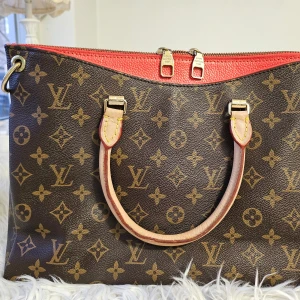 Monogram handväska från Louis Vuitton - Säljer en snygg handväska från Louis Vuitton med klassiskt monogrammönster. Väskan har en brun bas med röda detaljer och dragkedja. Handtagen är i ljust skinn och insidan är klädd i röd textil. Perfekt för dig som vill ha en stilren och lyxig accessoar. Finns inget kvitto eller äkthet. Kolla upp på koden bara. Tack