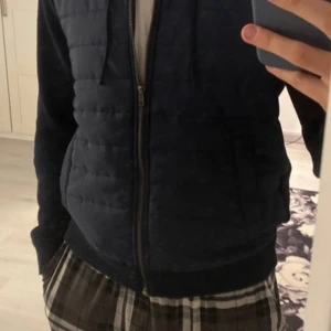 Mörkblå quiltad jacka med dragkedja - Säljer en mörkblå quiltad jacka med dragkedja. Jackan har långa ärmar och ribbade muddar. Perfekt för kyligare dagar med sin stilrena design.