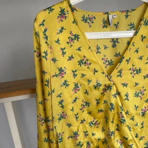 Omlottblus blommor - Gul omlottblus i silkigt material med blommönster. Storlek 36, från nelly. Fina snörningsdetaljer i ärmarna. Toppen skick💛💐