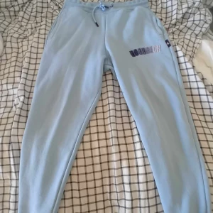 Ljusblå mjukisbyxor från Hoodrich - Säljer ett par ljusblå mjukisbyxor från Hoodrich. De är superbekväma och har en snygg broderad logga på sidan. Byxorna har en dragsko i midjan för perfekt passform. Perfekta för en chill dag hemma eller en avslappnad dag ute.