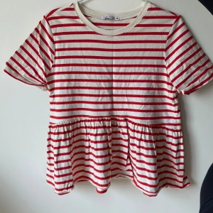 Randig topp från Zara - Säljer en superfin randig topp från Zara i rött och vitt. Den har korta ärmar och en söt volangdetalj nedtill som ger en extra touch. Perfekt för en avslappnad sommarlook!