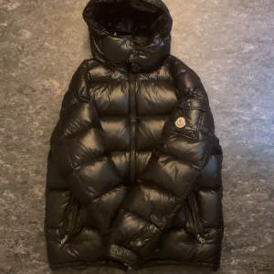 Svart pufferjacka från Moncler - Säljer min Moncler jacka eftersom jag inte behöver den längre. Skick 6-7/10 Ena dragkedjan tillfickan har gått sönder och fickan till höger fick ett hål som lätt går o fixa.