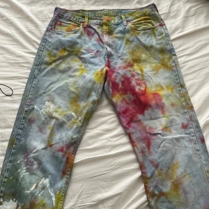 Färgglada Levis jeans - Säljer ett par unika och färgglada Levis jeans med ett coolt, färgstänkt mönster i rött, gult och grönt. Jeansen har en klassisk passform och är perfekta för att sticka ut i mängden. De är i bra skick och redo för en ny ägare.