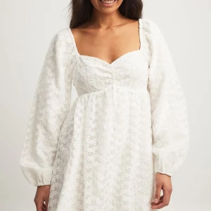 Vit blommig klänning från NA-KD - Säljer en söt vit klänning från NA-KD med blommigt mönster och långa ärmar. Klänningen har en v-ringad design och är perfekt för sommarens alla tillfällen. Den är gjord i ett lätt och luftigt material som ger en romantisk känsla. Helt slutsåld online 🎀 